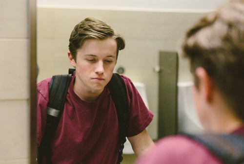 Teen looks at himself in bathroom mirror